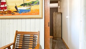 Un couloir avec une chaise en bois, un tableau représentant un paysage marin et une armoire en bois.