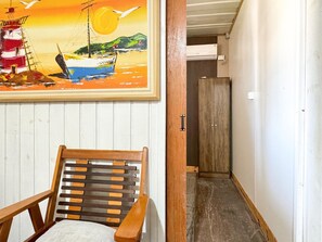Un pasillo con una silla de madera, un cuadro de un paisaje marino y un armario de madera.