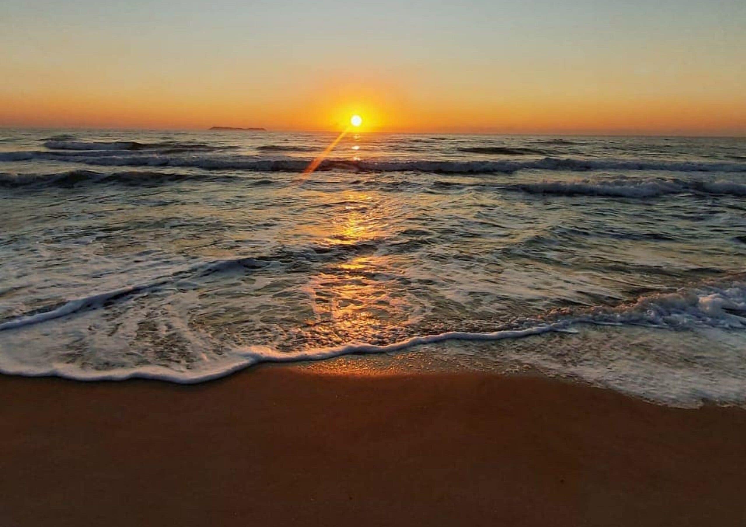 A beach with waves and a sunset.