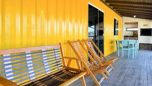 Un espace extérieur abrité, doté de bancs et de chaises en bois, d’un plancher en bois et d’un mur jaune.