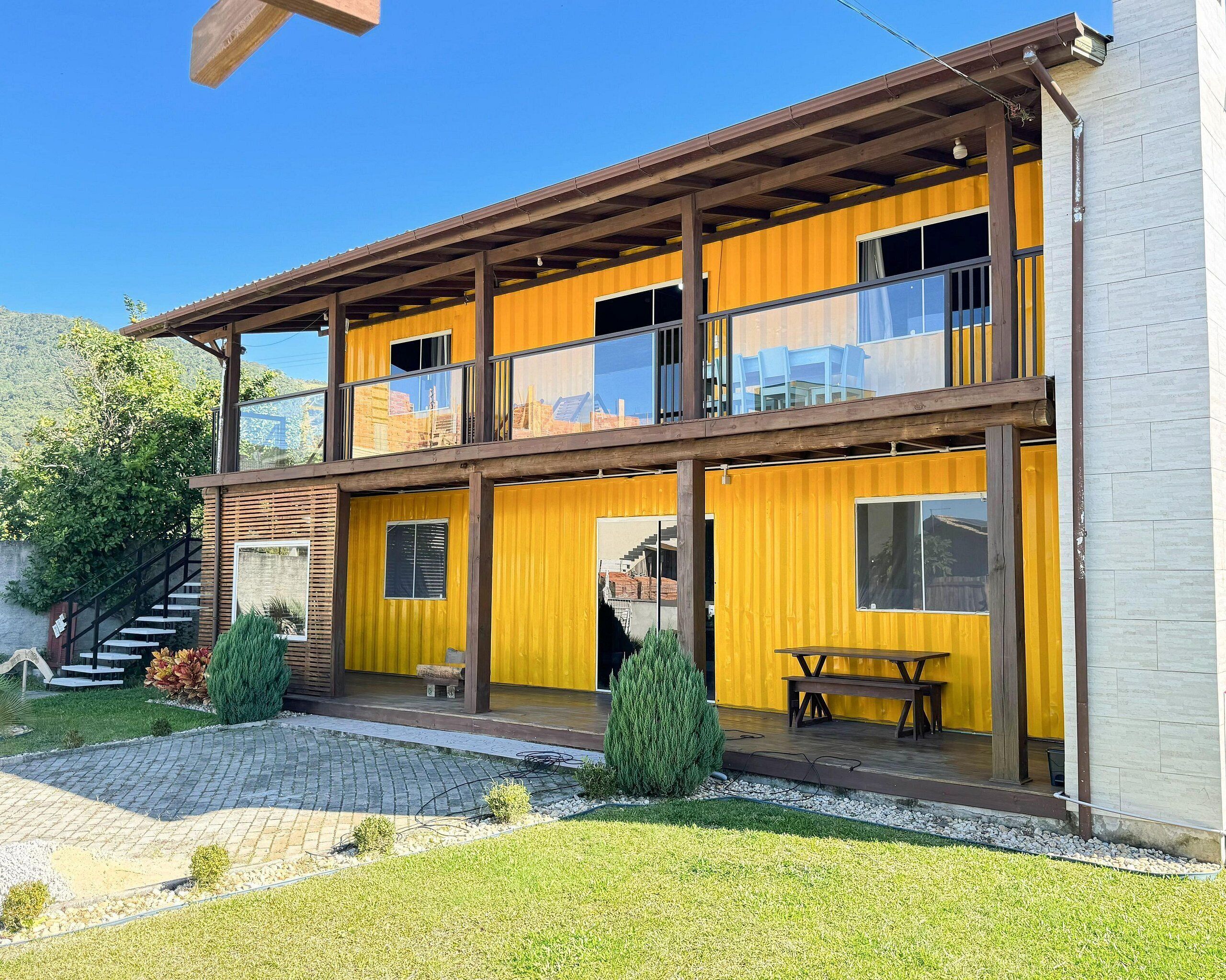 A two-story building with a yellow exterior, large windows, and a wooden balcony.