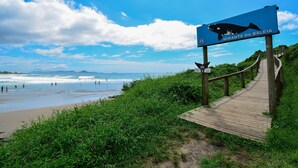 A wooden boardwalk leading to a beach with a sign indicating a whale watching spot. - Contêiner Exclusivo - Praia da Gamboa (Garopaba)