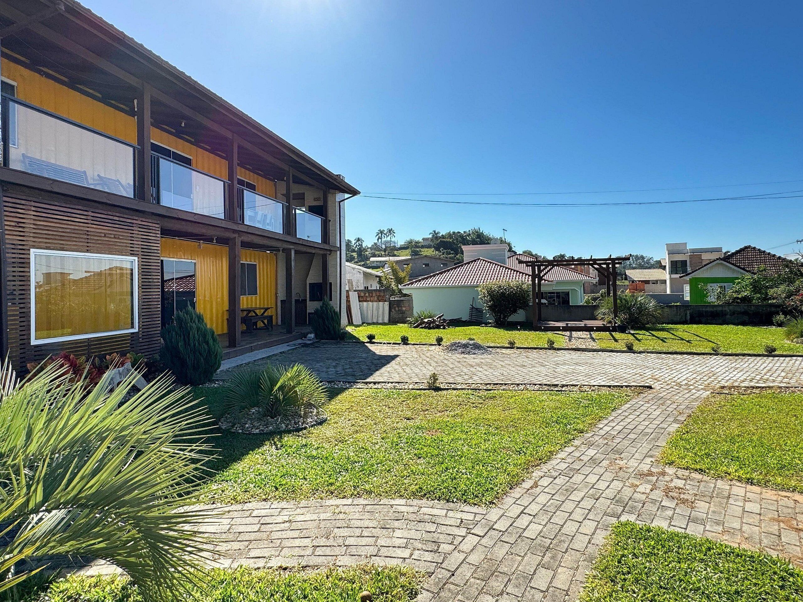 Um edifício moderno de dois andares com grandes janelas, um alpendre coberto e um pátio pavimentado com gramado e caminhos.