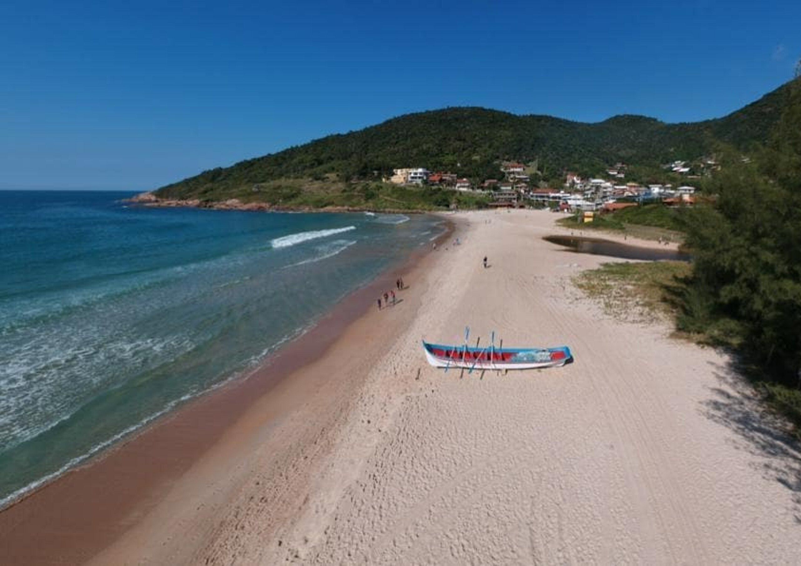 A beach with a boat on the sand, a clear sky, and a hilly background.