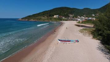 Uma praia com um barco na areia, céu claro e montanhas ao fundo.