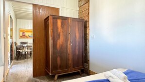 A room with a bed, a wooden wardrobe, and a dining area with a table and chairs. - Contêiner Exclusivo - Praia da Gamboa (Garopaba)