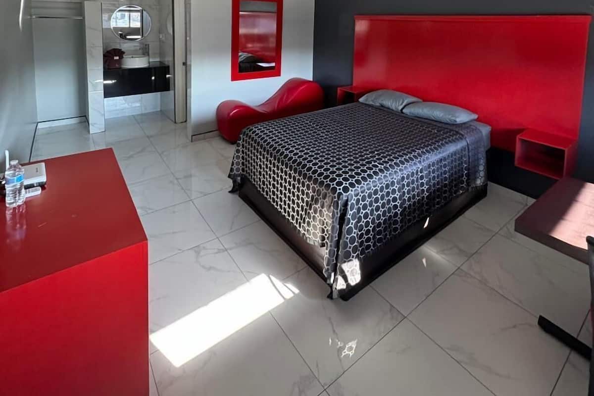 A modern bedroom with a bed, a red accent wall, a ceiling fan, and a red desk.
