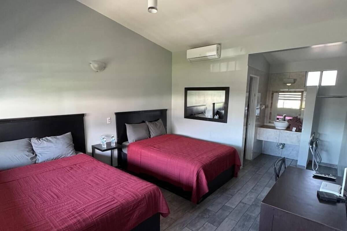 A hotel room with two beds, a desk, a mirror, and a bathroom visible through an open door.