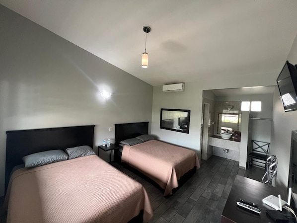 A hotel room with two beds, a desk, a chair, a TV, and a bathroom with a sink and mirror. - HOTEL MOTEL LUNA PARK (Tijuana)