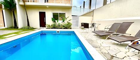 A swimming pool with lounge chairs and a small garden area.