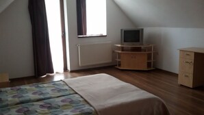 A bedroom with a bed, a TV on a wooden stand, a radiator, and a window with curtains. - Casa Dancs (Covasna)