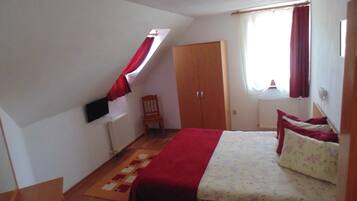 Un dormitorio con cama, armario de madera, radiador, ventana con cortinas y una pequeña silla.