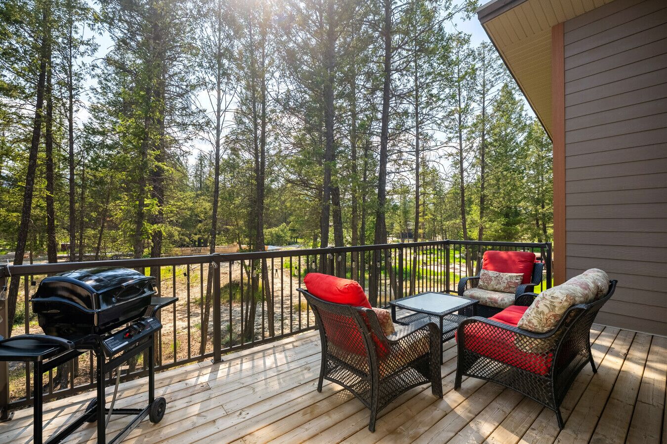 A wooden deck with outdoor furniture, a grill, and a view of a forest.