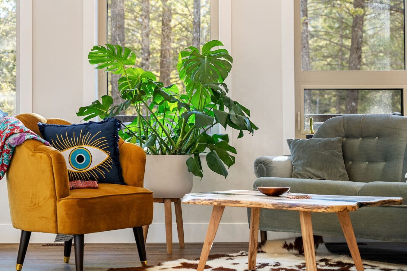 Uma sala de estar moderna com uma poltrona amarela, um sofá cinzento, uma mesa de centro de madeira e uma grande planta verde.