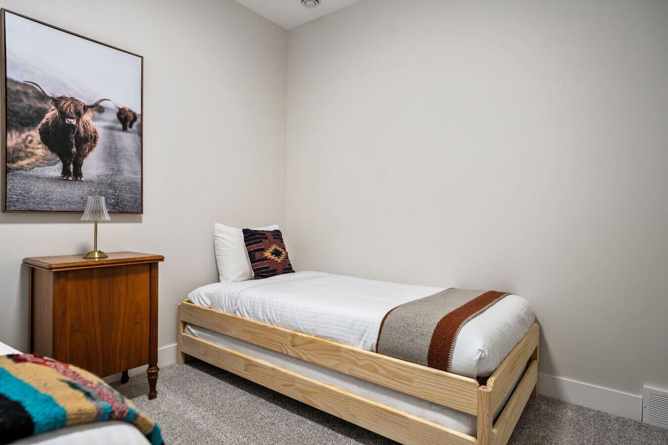 Un dormitorio con una cama de madera, una mesita de noche, una lámpara y un cuadro en la pared.