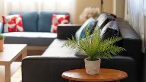 A modern living room with a sofa, a small round wooden table, and a potted plant. - Fabulous 3bdrm Home w/parking! (Highland Falls)