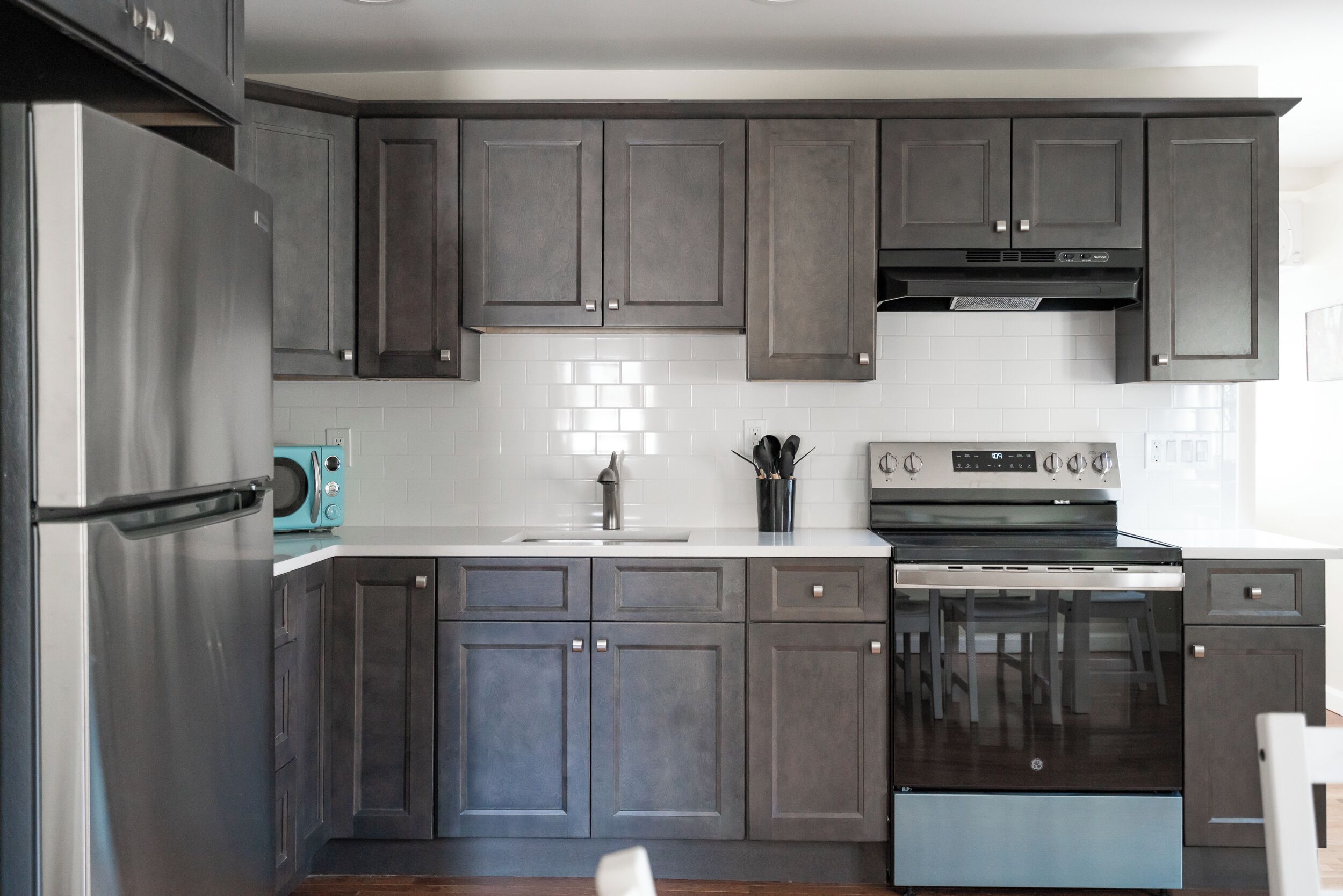 A modern kitchen with dark grey cabinets, a stainless steel refrigerator, a built-in oven, and a microwave.
