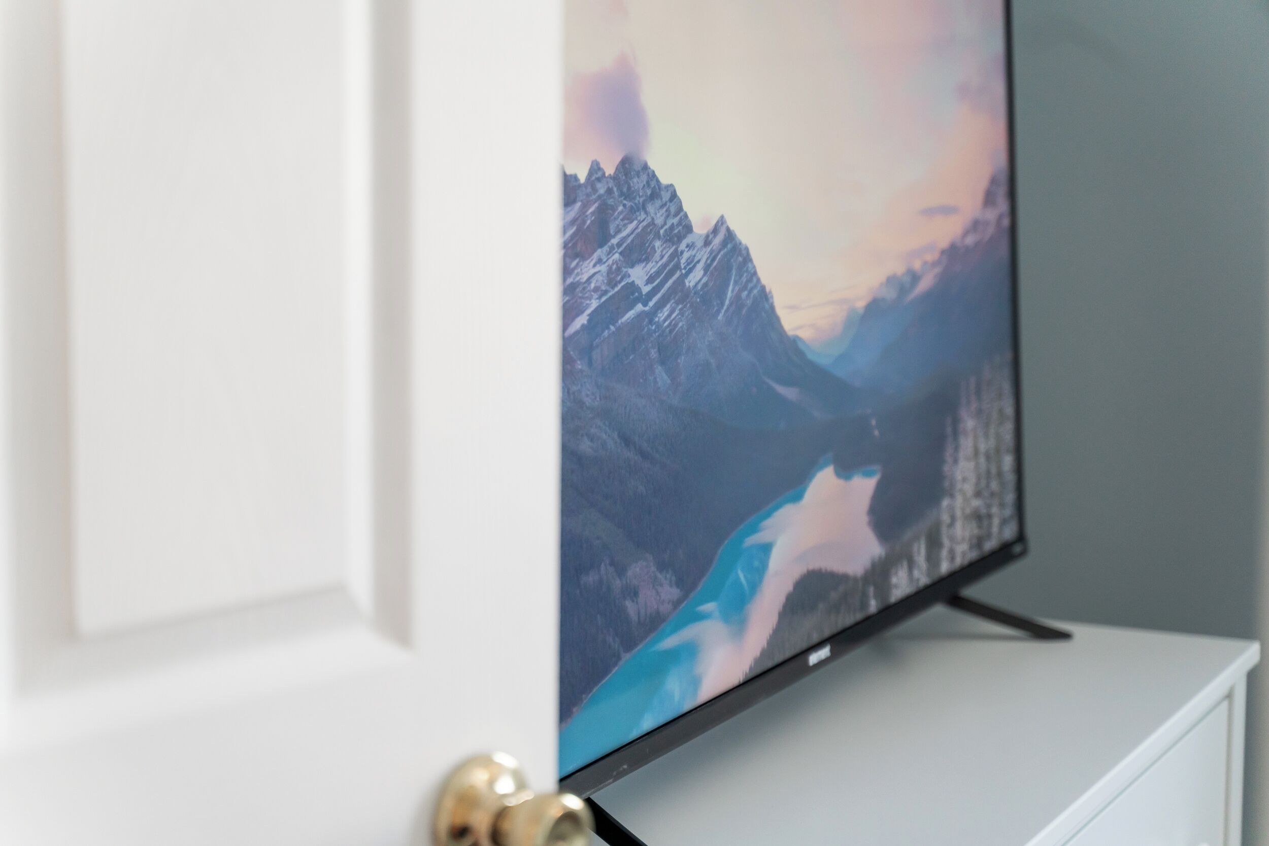 A flat-screen TV mounted on a white cabinet with a mountain landscape displayed on the screen.