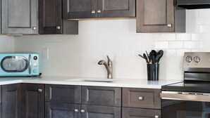 A kitchen with dark cabinets, a white tiled backsplash, a blue microwave, a stainless steel faucet, and a coffee maker. - Fabulous 3bdrm Home w/parking! (Highland Falls)