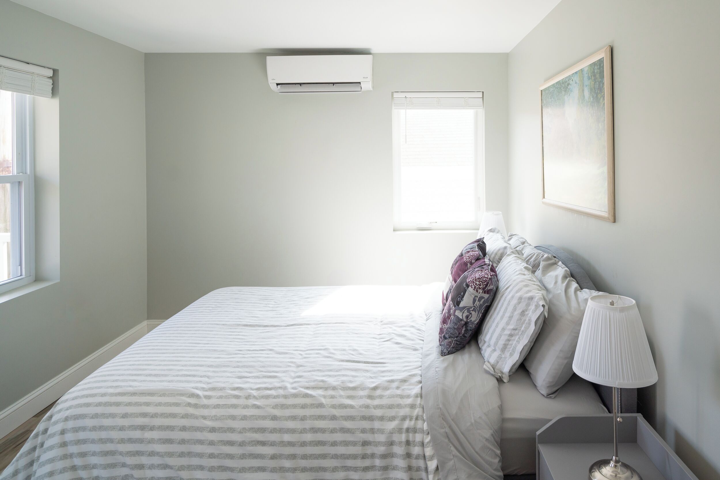 A bedroom with a bed, a nightstand, a lamp, and a painting on the wall.