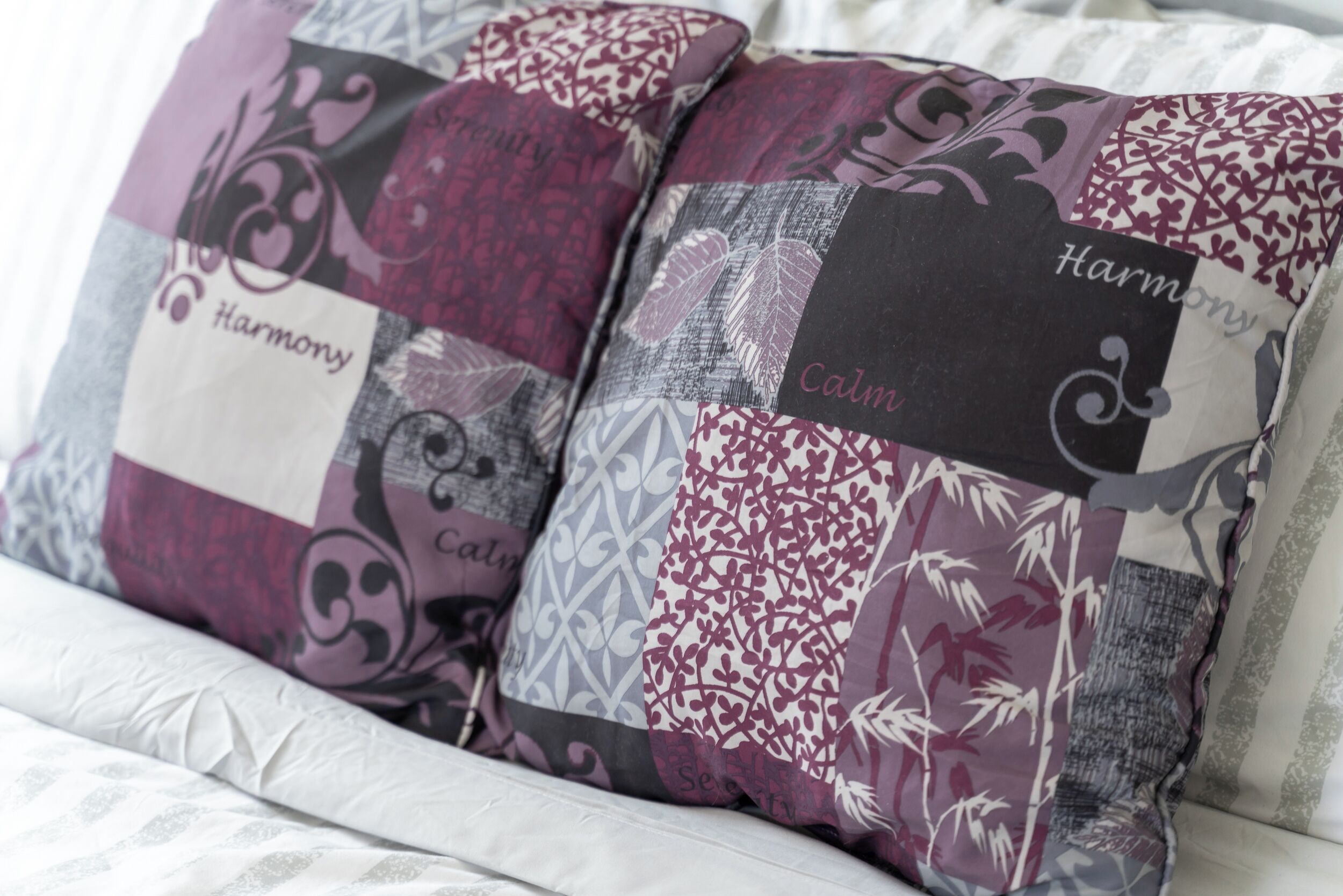 Un letto con lenzuolo bianco e due cuscini decorativi con motivi a patchwork e le scritte “Harmony” e “Calm”.