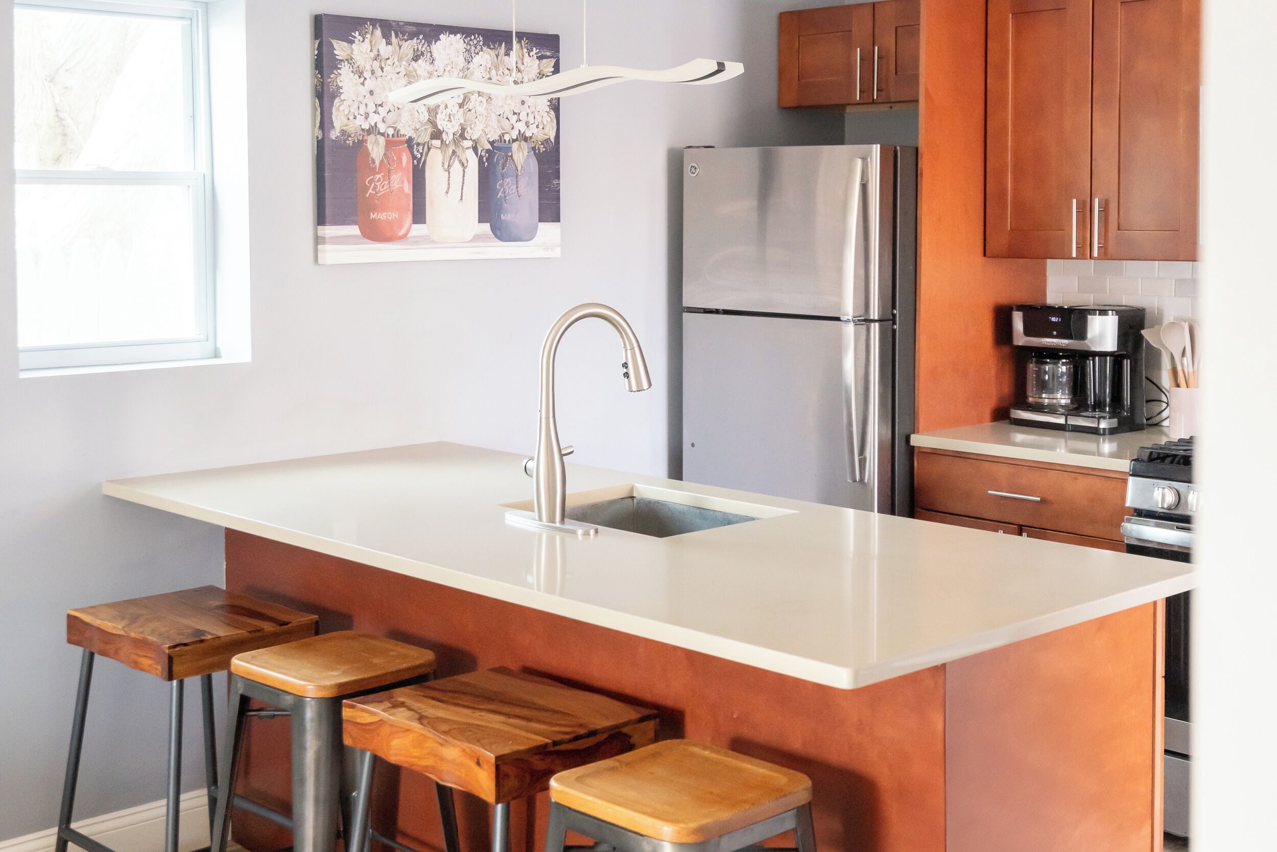 A kitchen with a large island, stainless steel appliances, wooden stools, and a coffee maker.