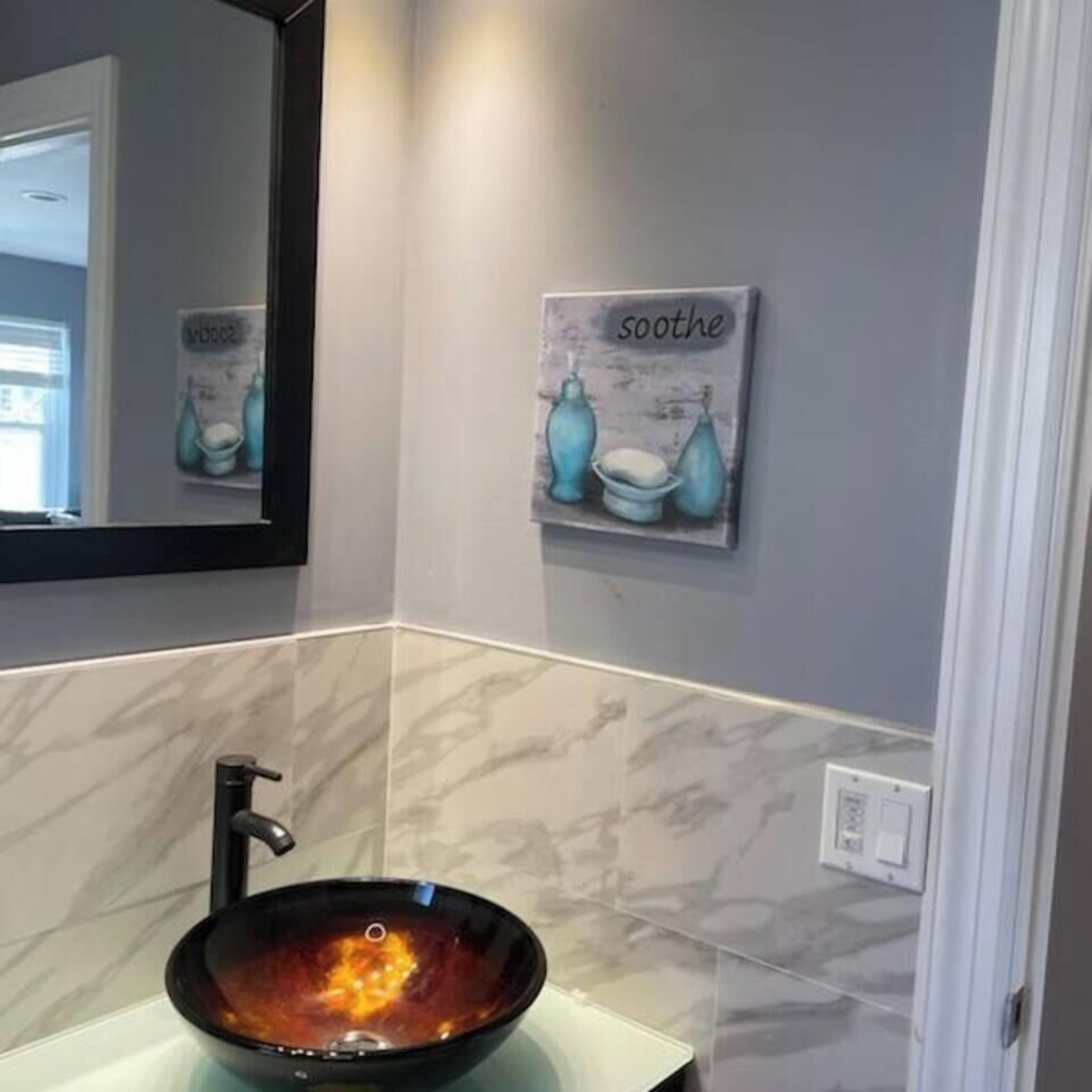 A bathroom with a black vessel sink, a mirror, and a wall-mounted artwork with the word "soothe".