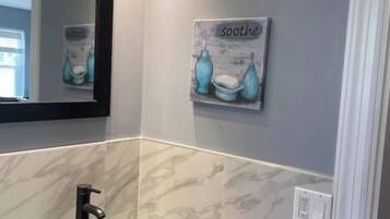 A bathroom with a black vessel sink, a mirror, and a wall-mounted artwork with the word "soothe".