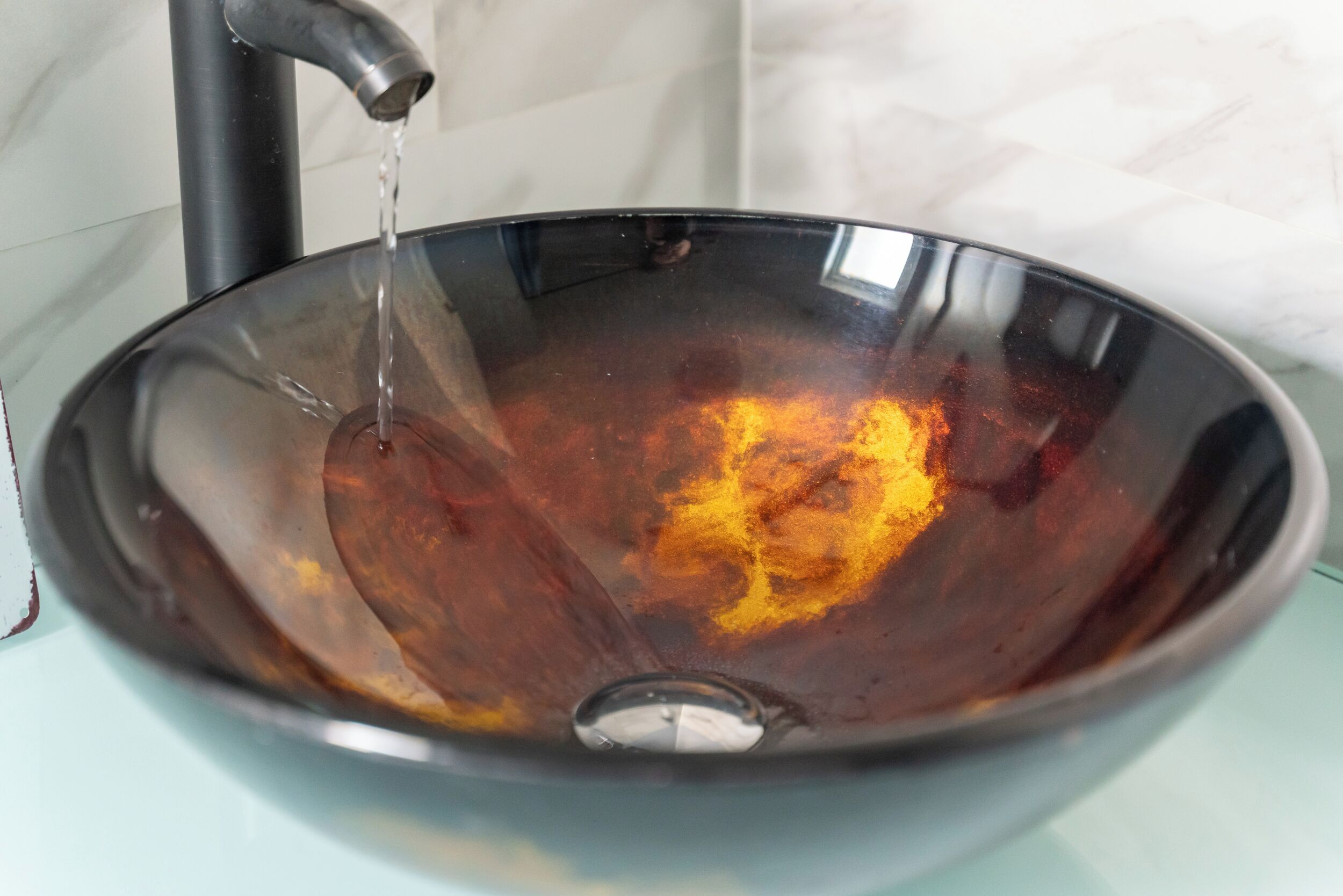 A metallic bowl sink with water running from a faucet.
