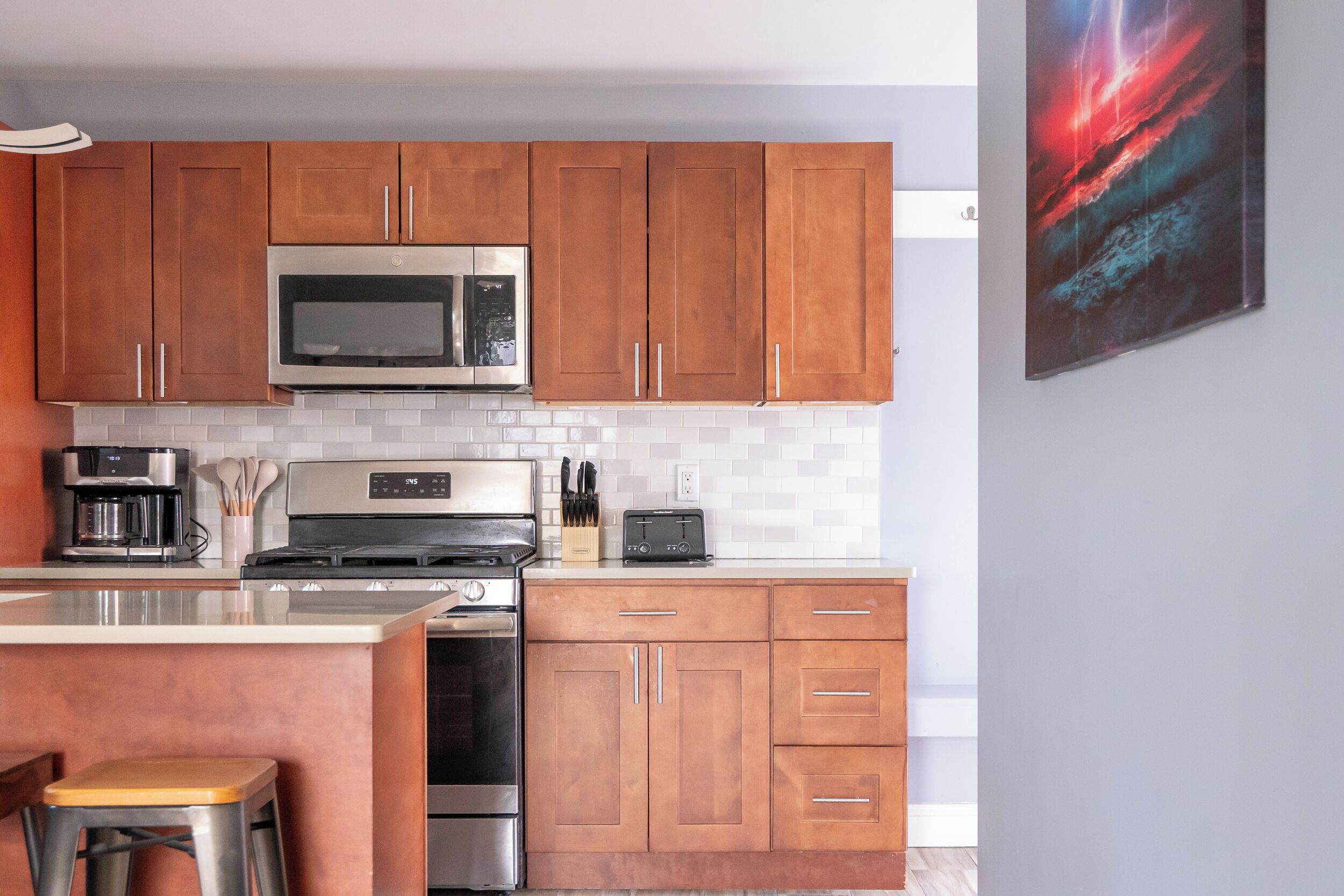 Een moderne keuken met houten kastjes, roestvrijstalen apparatuur en een witte betegelde achterwand.