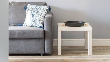 Un divano grigio con un cuscino decorato e un comodino bianco con un vassoio nero.