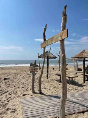 Ein Strand mit Holzschildern, darunter ein Schild mit der Aufschrift 'LA PAULOTTE', und einer Holzterrasse.