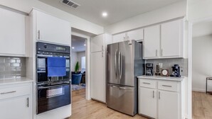A modern kitchen with white cabinets, a stainless steel refrigerator, a built-in oven, and a coffee maker.