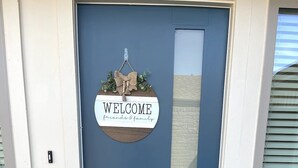 A blue door with a welcome sign and a doormat that reads "COME AS GUESTS LEAVE AS FRIENDS".