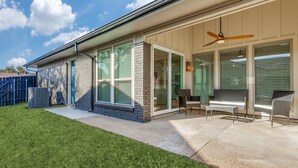 A modern house with a patio, large windows, and a ceiling fan.
