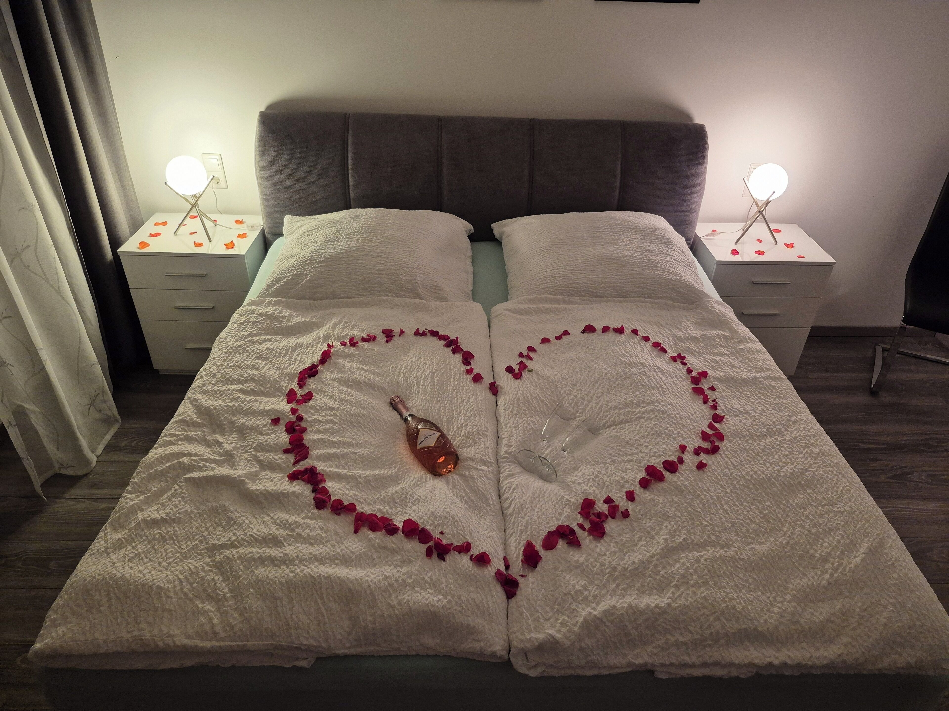 Un lit décoré de pétales de roses disposés en forme de cœur et une bouteille de champagne.