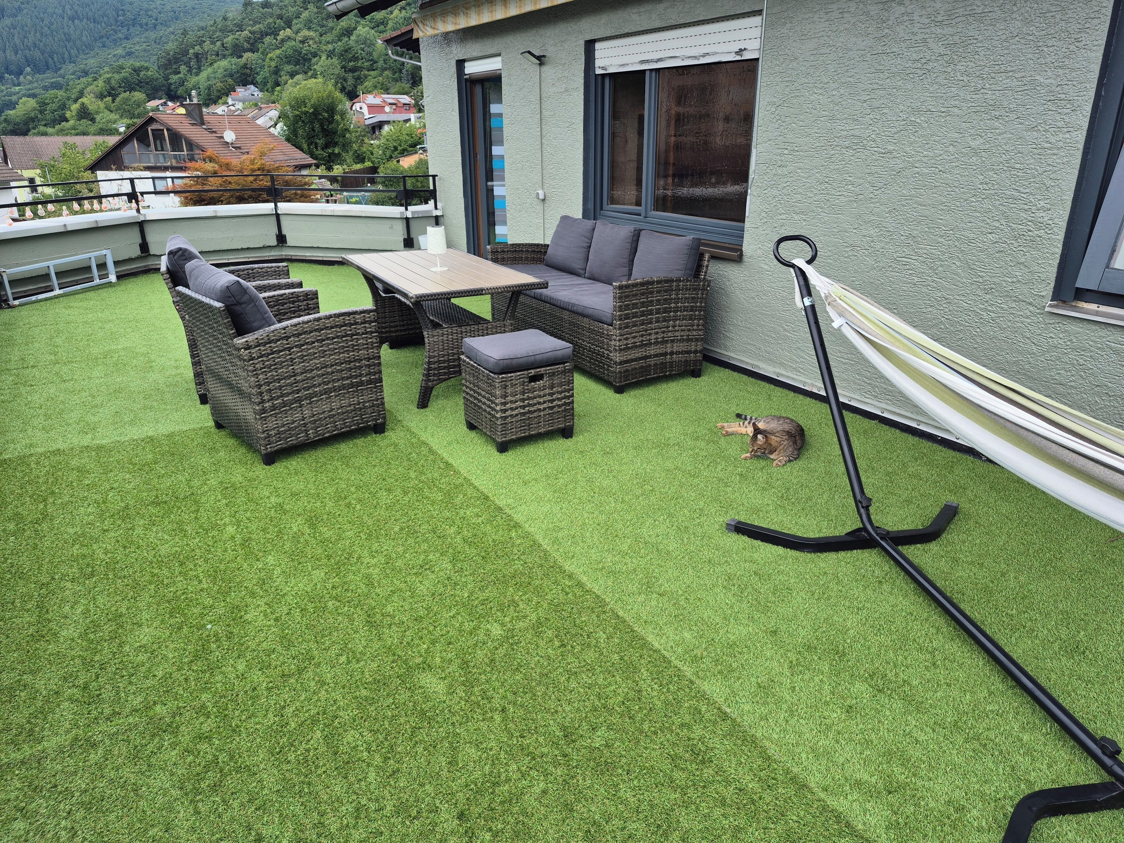 Een terras met kunstgras, rieten meubels en een hangmat.