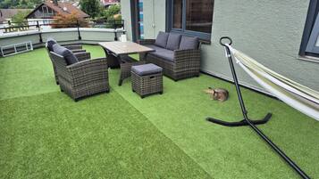 Een terras met kunstgras, rieten meubels en een hangmat.