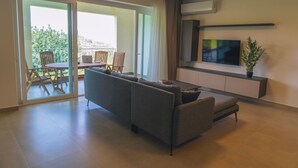 Una sala de estar moderna con un sofá, un televisor y un balcón con sillas y una mesa.
