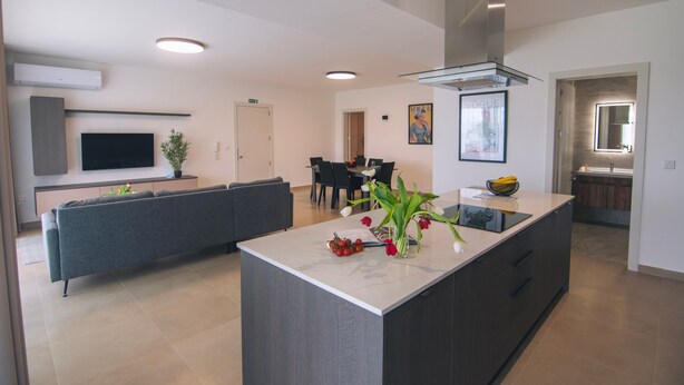 Una cocina moderna con una isla central, armarios oscuros y una zona de comedor con mesa y sillas.