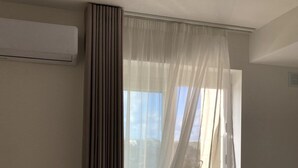 Ein Zimmer mit einer großen SchiebeglasTür, die auf einen Balkon führt, einer hohen Klimaanlage an der Wand und einer Steckdose am Boden.