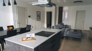 Une cuisine moderne dotée d’un îlot central, de meubles de rangement aux couleurs sombres et d’un coin repas avec des chaises et une table.