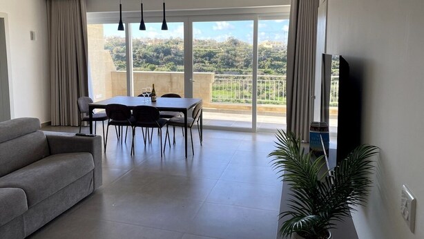 A modern living room with a sofa, dining table, chairs, and a TV. - The Valley Collection - Suite B23 (Ix-Xagħra)