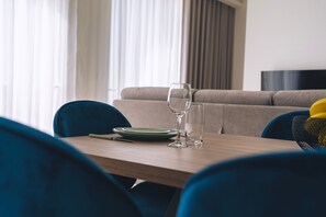 Un área de comedor con una mesa de madera, dos sillas, un plato verde, una copa de vino y un vaso de agua.