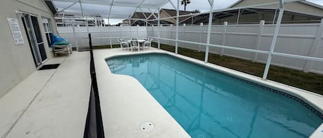 A rectangular pool with a white deck and a covered area.