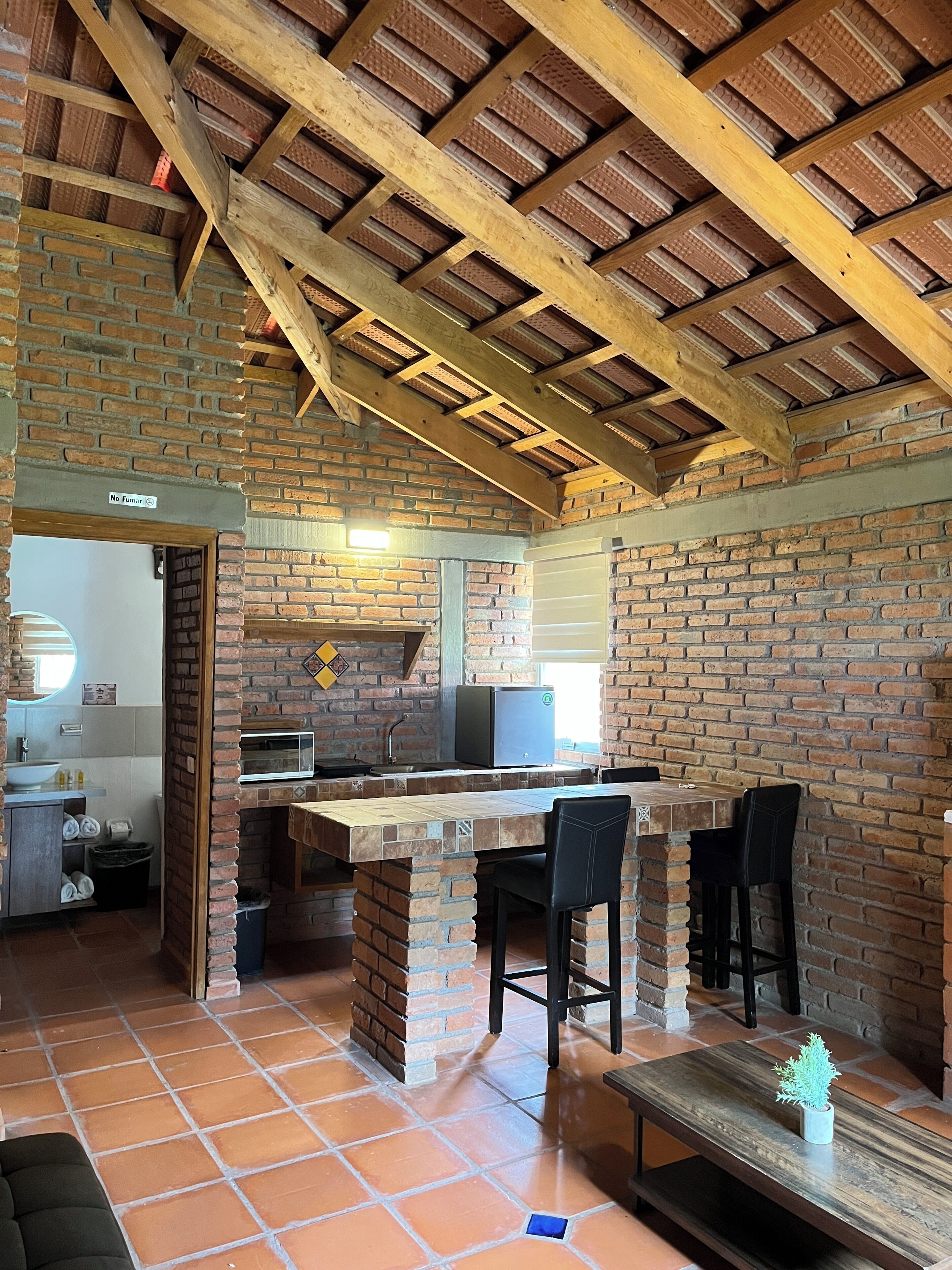 A rustic kitchen with exposed brick walls, a wooden ceiling, and a central island with bar stools.