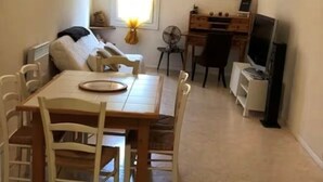 A compact living space with a dining area, a sofa, a TV, and a small desk. - VILLAGE HOUSE FOR RENT (Torreilles)