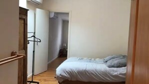 A narrow hallway with a wooden floor leading to a bedroom with a bed and a hanging light fixture. - VILLAGE HOUSE FOR RENT (Torreilles)