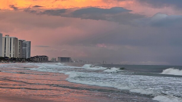 A beach with waves and a city skyline in the background.