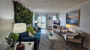 Un salon avec un canapé bleu, une table basse, un téléviseur et un mur décoré de plantes et de guirlandes lumineuses.